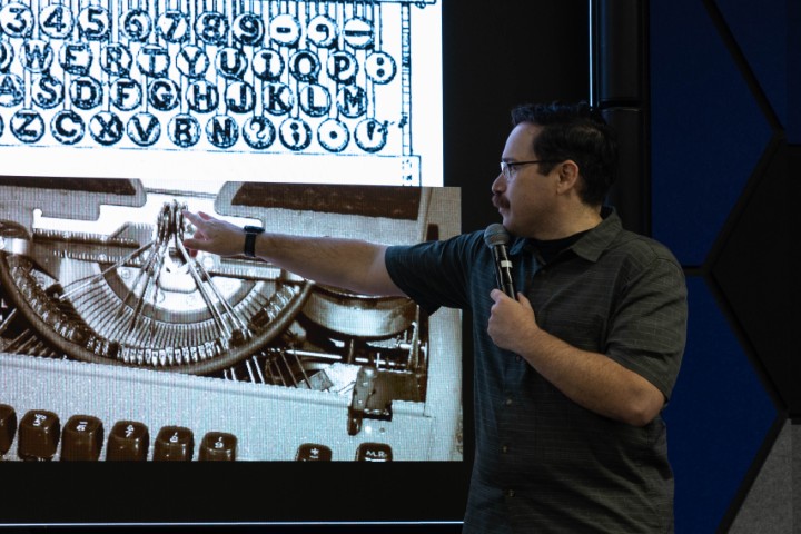 A presenter pointing at a projection of a typewriter.